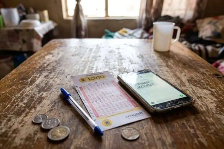 image of a lotto ticket on a table with South African rand coins and a smartphone on a table.