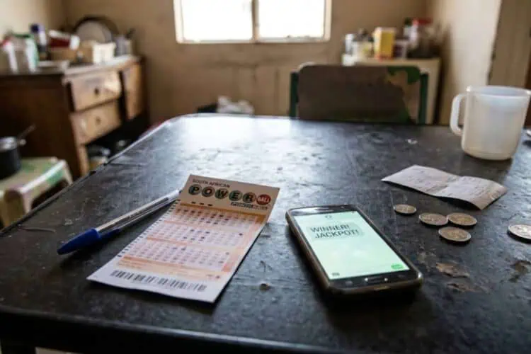 image of a powerball ticket on a table with South African rand coins and a smartphone on a table.